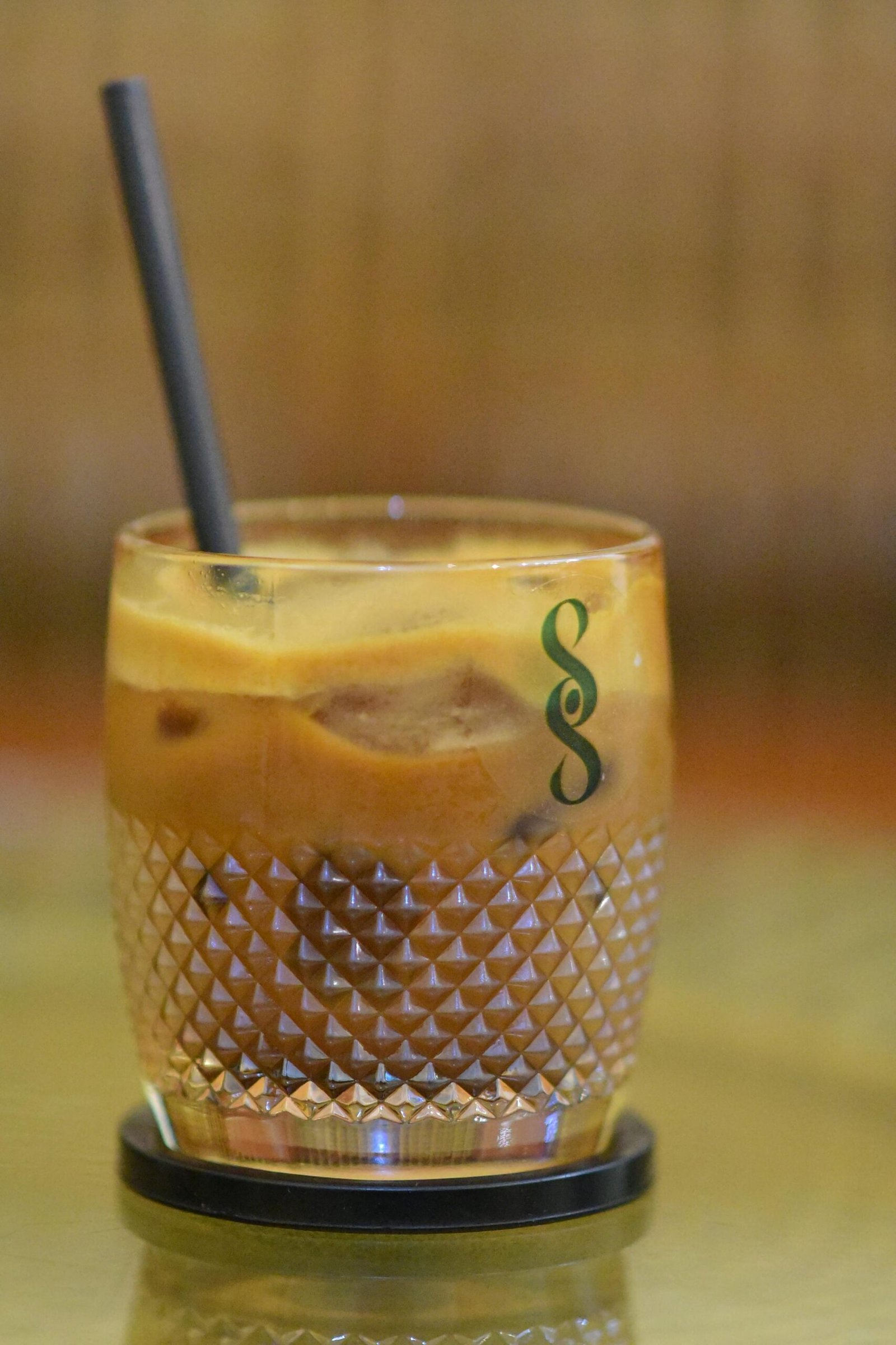 Iced coffee served in a textured glass with a straw, featuring a rich, creamy layer.